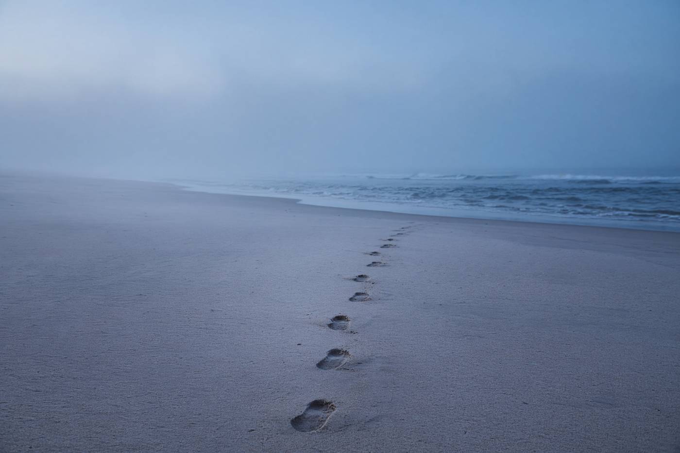 Empty beach at blue hour with a line of wet footprints toward the water